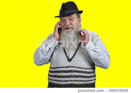 Portrait of bearded senior man with hat and beard talking on phone. Isolated on yellow background. 106039089