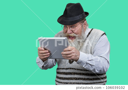 Portrait of excited senior man with tablet pc. Bearded grandpa with his mouth closed. Isolated on green. 106039102