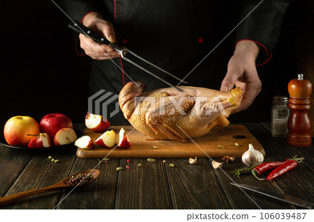 Cooking roast duck in the kitchen of a restaurant by a cook. Raw duck with apples on a cutting board. Fork in the chef's hand Cooking roast duck in the kitchen of a restaurant by a cook. Raw duck with apples on a cutting board. Fork in the chef's hand 106039487