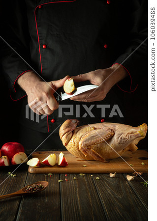 The chef cuts apples with a knife to add to raw duck before roasting in the oven. Cooking a national dish in the kitchen of a restaurant by the hands of a cook The chef cuts apples with a knife to add to raw duck before roasting in the oven. Cooking a national dish in the kitchen of a restaurant by the hands of a cook 106039488