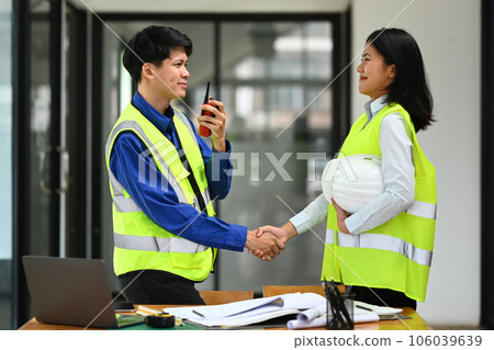 Foreman and engineer woman holding helmets and shaking hands after successful meeting in the office. 106039639