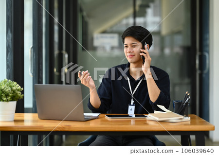 Handsome male financial advisor looking at laptop screen, talking on mobile phone with client 106039640
