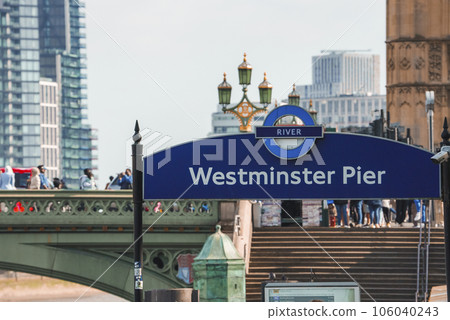 Westminster pier sign in capital city. Tourists walking on bridge with sky in background. Text on blue signboard at riverbank during sunny day. 106040243