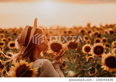 Woman in Sunflower Field: Happy girl in a straw hat posing in a vast field of sunflowers at sunset, enjoy taking picture outdoors for memories. Summer time. 106044896