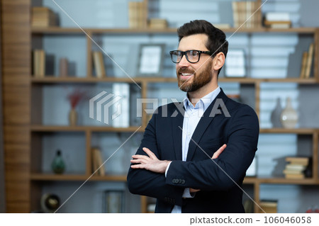 Portrait of successful mature boss, senior businessman in glasses and business suit looking away and smiling, man with crossed arms working inside modern office building. Portrait of successful mature boss, senior businessman in glasses and business suit looking away and smiling, man with crossed arms working inside modern office building. 106046058