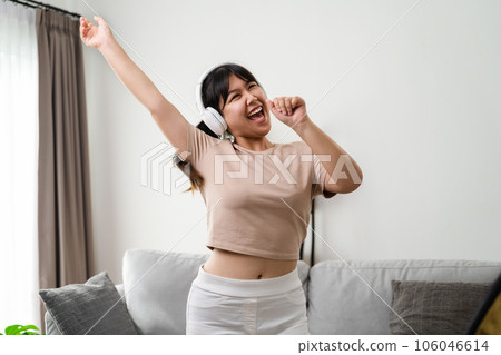 Young woman listen to music with headphone and dance in the living room at home. 106046614