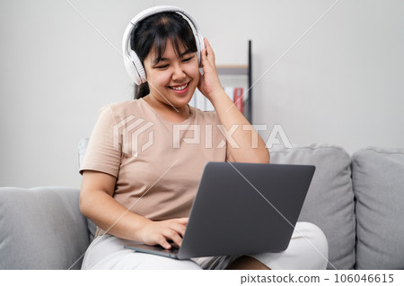 Young woman listen to music with headphone and use laptop computer for study, work, relax sitting on the sofa at home. 106046615