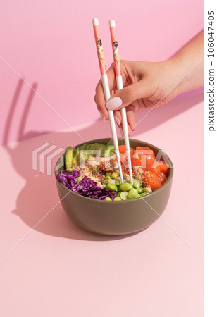 Hands eating poke bowl with salmon on pink background 106047405
