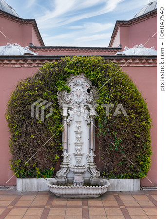 Marble fountain surrounded by lush greenery in pink stone wall of Hagia Sophia Hurrem Sultan Bathhouse, Istanbul, Turkey 106047540