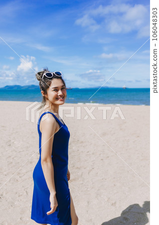 Vertical portrait of happy woman in. blue dress walking on the beach. Vertical portrait of happy woman in. blue dress walking on the beach. 106048303