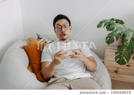 Man playing mobile game making funny intense face in the living room. 106048659