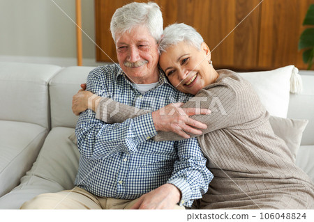 Senior adult mature couple hugging at home. Mid age old husband and wife embracing with tenderness love enjoying sweet bonding wellbeing. Grandmother grandfather together. Family moment love and care 106048824