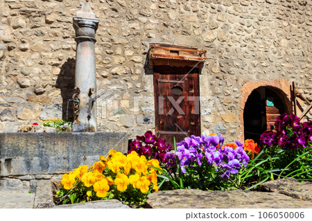 Fountain with drinking water in courtyard of Chillon castle. Flowerbed of colorful pansies (viola tricolor) on a foreground Fountain with drinking water in courtyard of Chillon castle. Flowerbed of colorful pansies (viola tricolor) on a foreground 106050006