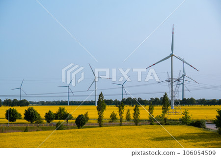 Wind turbine on grassy yellow field against cloudy blue sky in rural area during sunset. Offshore windmill park with stormy clouds in farmland Poland Europe. Wind power plant generating electricity Wind turbine on grassy yellow field against cloudy blue sky in rural area during sunset. Offshore windmill park with stormy clouds in farmland Poland Europe. Wind power plant generating electricity 106054509