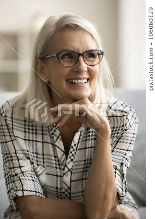 Cheerful beautiful mature woman in glamour glasses sitting on couch Cheerful beautiful mature woman in glamour glasses sitting on couch 106060129