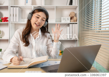 Beautiful young asian woman watching live video or video call of teacher teaching on laptop in her home, Take notes of important conversations and messages during the teacher's teaching. 106061397