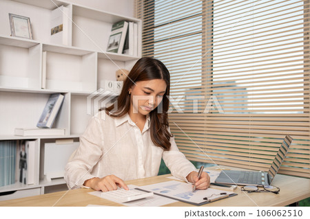 Asian woman working at home, Press the calculator to calculate the income - expenses of the house and use the laptop to record the information and check the accuracy, Home lifestyle. 106062510
