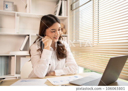 Woman using laptop to work or do homework at home with smiling face in her office, Creating happiness at work with a smile, Live performance or vdo call with laptop, Work from home. Woman using laptop to work or do homework at home with smiling face in her office, Creating happiness at work with a smile, Live performance or vdo call with laptop, Work from home. 106063801