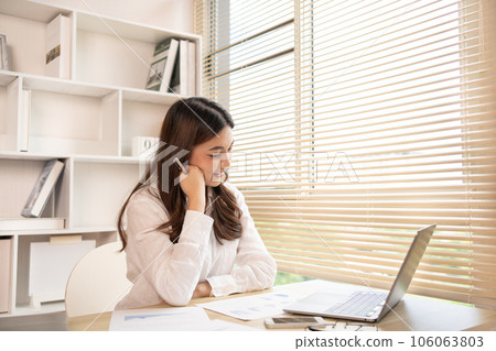 Woman using laptop to work or do homework at home with smiling face in her office, Creating happiness at work with a smile, Live performance or vdo call with laptop, Work from home. 106063803