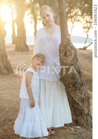 Portrait of two sisters, kid and teenage girl in white clothes against background of park Portrait of two sisters, kid and teenage girl in white clothes against background of park 106063823