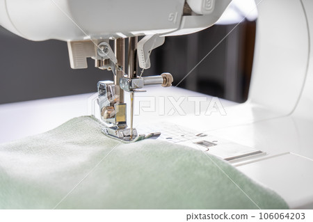 Modern sewing machine presser foot with green fabric and thread, closeup, macro 106064203