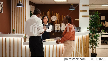 Friendly smiling asian receptionist handing contract on tablet for african american tourists to sign after upgrading room amenities. Happy relaxed guests on vacation trip checking in stylish hotel 106064655