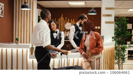 Husband and wife on honeymoon trip requesting special room amenities from asian receptionist in hotel lobby. Helpful concierge personnel presenting holiday package deal to couple in luxury resort Husband and wife on honeymoon trip requesting special room amenities from asian receptionist in hotel lobby. Helpful concierge personnel presenting holiday package deal to couple in luxury resort 106064661