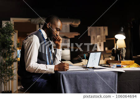 Expert couturier handdrawing sketch of upcoming custom made sartorial collection in atelier shop workspace. Creative fashion designer creating bespoke garment after looking for inspiration online 106064694