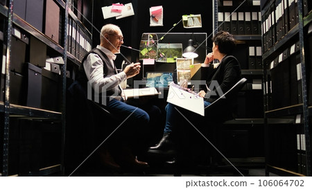 Partners review surveillance photos and classified case information, reading documents to connect the dots. Team of detectives evaluating forensic evidence authenticity, crime discovery. Partners review surveillance photos and classified case information, reading documents to connect the dots. Team of detectives evaluating forensic evidence authenticity, crime discovery. 106064702