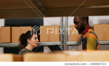 Team of supervisors checking stock list and doing inventory in storage room, diverse people verifying logistics for merchandise distribution. Man and woman reviewing products. Handheld shot. Team of supervisors checking stock list and doing inventory in storage room, diverse people verifying logistics for merchandise distribution. Man and woman reviewing products. Handheld shot. 106064722