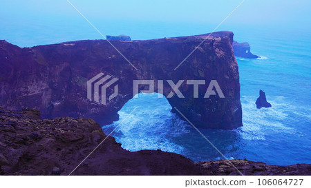 Dyrholaey peninsula icelandic coastline with rocky arch gate and massive cliffs, foggy freezing winter. Beautiful iceland nature and ocean shore with scenic landscapes. Handheld shot. Dyrholaey peninsula icelandic coastline with rocky arch gate and massive cliffs, foggy freezing winter. Beautiful iceland nature and ocean shore with scenic landscapes. Handheld shot. 106064727