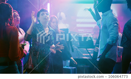 Happy friends having fun at nightclub, showing funky dance moves on dance floor and enjoying modern party. Man and woman dancing with group of people at discotheque, nightlife with music. Happy friends having fun at nightclub, showing funky dance moves on dance floor and enjoying modern party. Man and woman dancing with group of people at discotheque, nightlife with music. 106064773