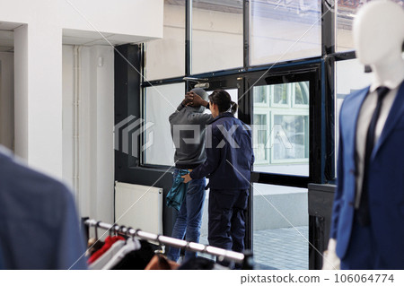 Worker putting thief to stay with arms raised while check for stolen items at boutique door. African american robber wearing hood and sunglassed, trying to steal fashionable clothes 106064774