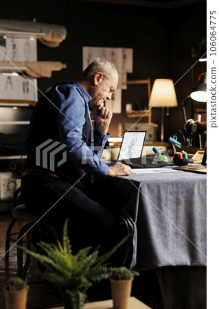 Senior couturier creating refined premium quality attire, looking online for inspiration. Elderly tailor trying to come up with ideas for upcoming custom made fashion collection 106064775
