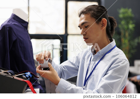 Asian client arranging formal wear accessories in modern boutique, putting belt on store shelf. Clothing store manager working with fashionable clothes in shopping centre. Fashion concept 106064812