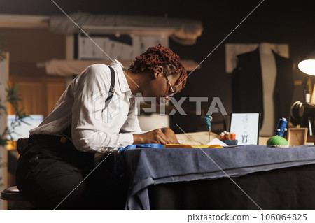 Creative african american dressmaker handdrawing sketch design for upcoming client comission in tailoring studio. Experienced skilled couturier creating bespoken refined garments 106064825