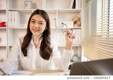 Woman using laptop to work or do homework at home with smiling face in her office, Creating happiness at work with a smile, Live performance or vdo call with laptop, Work from home. Woman using laptop to work or do homework at home with smiling face in her office, Creating happiness at work with a smile, Live performance or vdo call with laptop, Work from home. 106064827