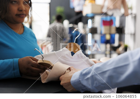 African american woman putting shirts on counter desk, before paying for stylish clothes in modern boutique. Cheerful shopper wanting new wardrobe, shopping for fashionable items and accessories 106064855