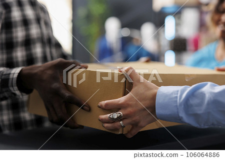 African american customer holding cardboard box at counter desk, after buying fashionable merchandise. Stylish man shopping for elegant clothes, discussing about material in modern boutique 106064886