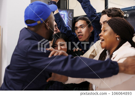 African man security guard pushing back crazy obsessed customers at shop entrance during Black Friday sale. Crowd of anxious diverse people shoppers breaking into shopping mall on Cyber Monday 106064893