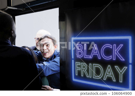 Security officer opening shopping mall entrance door on Black Friday. Crazy fanzy crowd of excited diverse people shoppers breaking into store to get best deals during seasonal sales 106064900