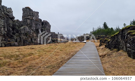 Rocky mountain range in arctic scenery, thingvellir national park with spectacular landscapes and massive cliffs in iceland. Rock formations creating hills in icelandic valley with walkway. Rocky mountain range in arctic scenery, thingvellir national park with spectacular landscapes and massive cliffs in iceland. Rock formations creating hills in icelandic valley with walkway. 106064937