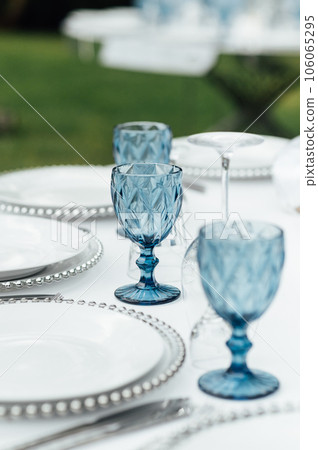 Open -air wedding banquet. The table is decorated with white plates and premium glasses for wine Open -air wedding banquet. The table is decorated with white plates and premium glasses for wine 106065295