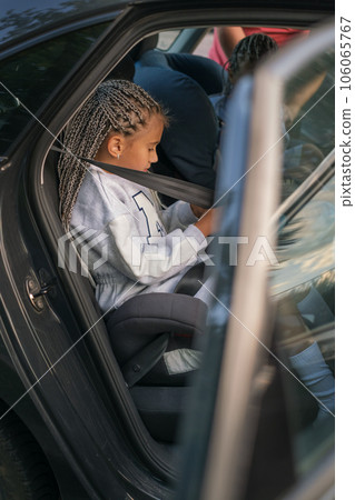 The girl in the car in the back seat is fastened with a seat belt on her own. The child knows about the importance of safe travel The girl in the car in the back seat is fastened with a seat belt on her own. The child knows about the importance of safe travel 106065767
