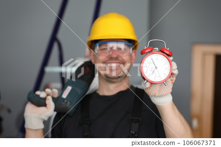Male builder helmet laughing showing alarm clock Male builder helmet laughing showing alarm clock 106067371