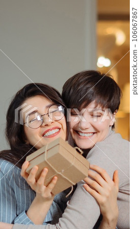 Young beautiful girl sitting in cafe with her friend and receiving a gift 106067867