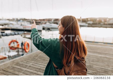 Redhead 30s women pointing finger. Woman Searching locations, walking along the waterfront, seaside. Redhead 30s women pointing finger. Woman Searching locations, walking along the waterfront, seaside. 106068138