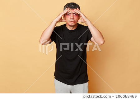 Sick sad man in black T-shirt with bruises and abrasions on his face isolated over beige background touching painful head frowning face has trauma after fighting. Sick sad man in black T-shirt with bruises and abrasions on his face isolated over beige background touching painful head frowning face has trauma after fighting. 106068469
