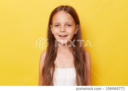 Pleased pretty smiling happy little girl with ponytails standing isolated over yellow background looking at camera with positive expression. 106068771