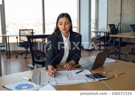 Focused female architect engineer working with documents project sitting desk in office 106072526